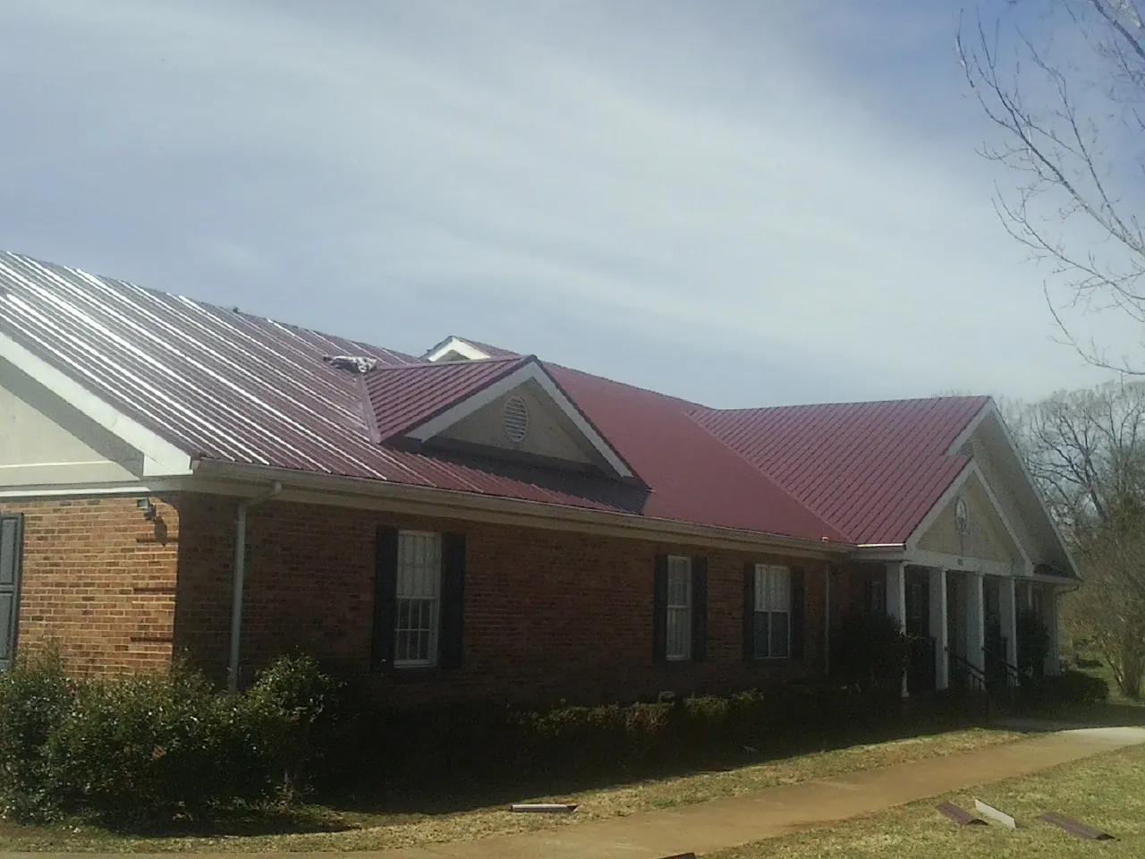 Red metal roof with gabled entries on a long brick building, from a Hail Damage Roof Repair job in New Berlin
