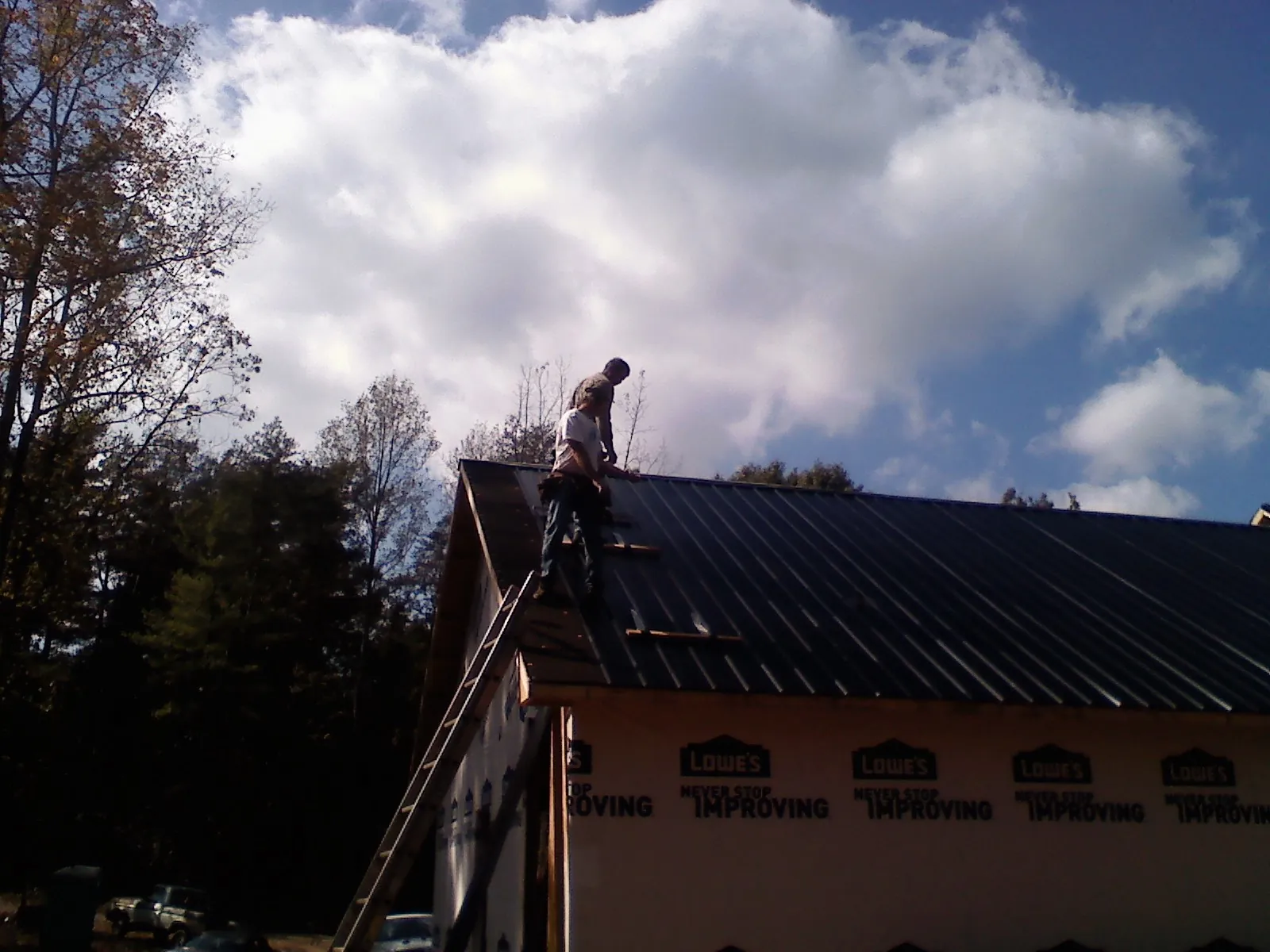 Roofer fastening dark metal panels high against a cloudy sky, from a Roof Inspection job in New Berlin