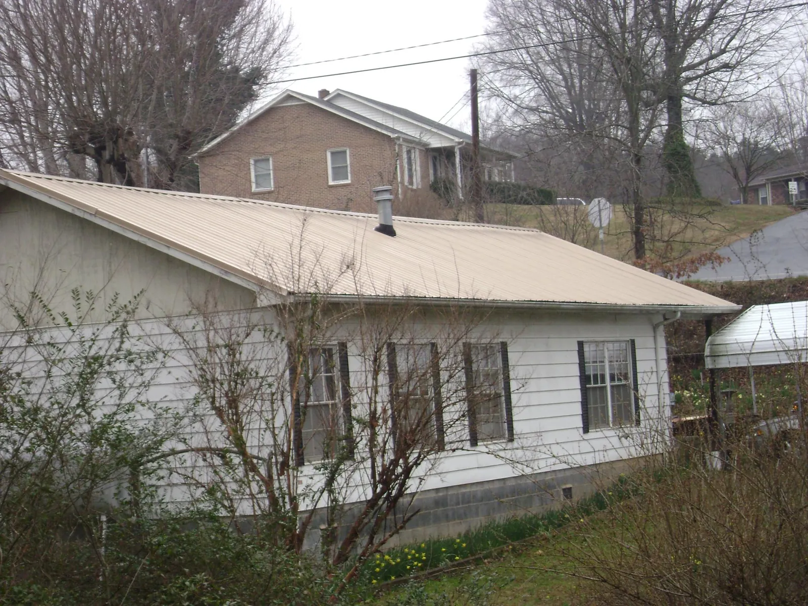 Tan metal roof on a white sided house set into a hillside — Commercial Roofing by Roofing Brothers in New Berlin